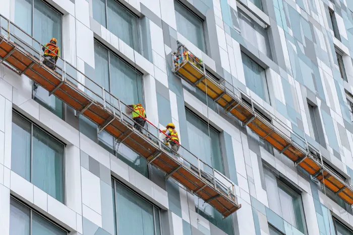 تیم اجرایی در حال نصب نمای خشک آلومینیومی بر روی برج مدرن با استفاده از داربست معلق — اجرای سیستم نمای خشک توسط گروه ساختمانی ساخَط